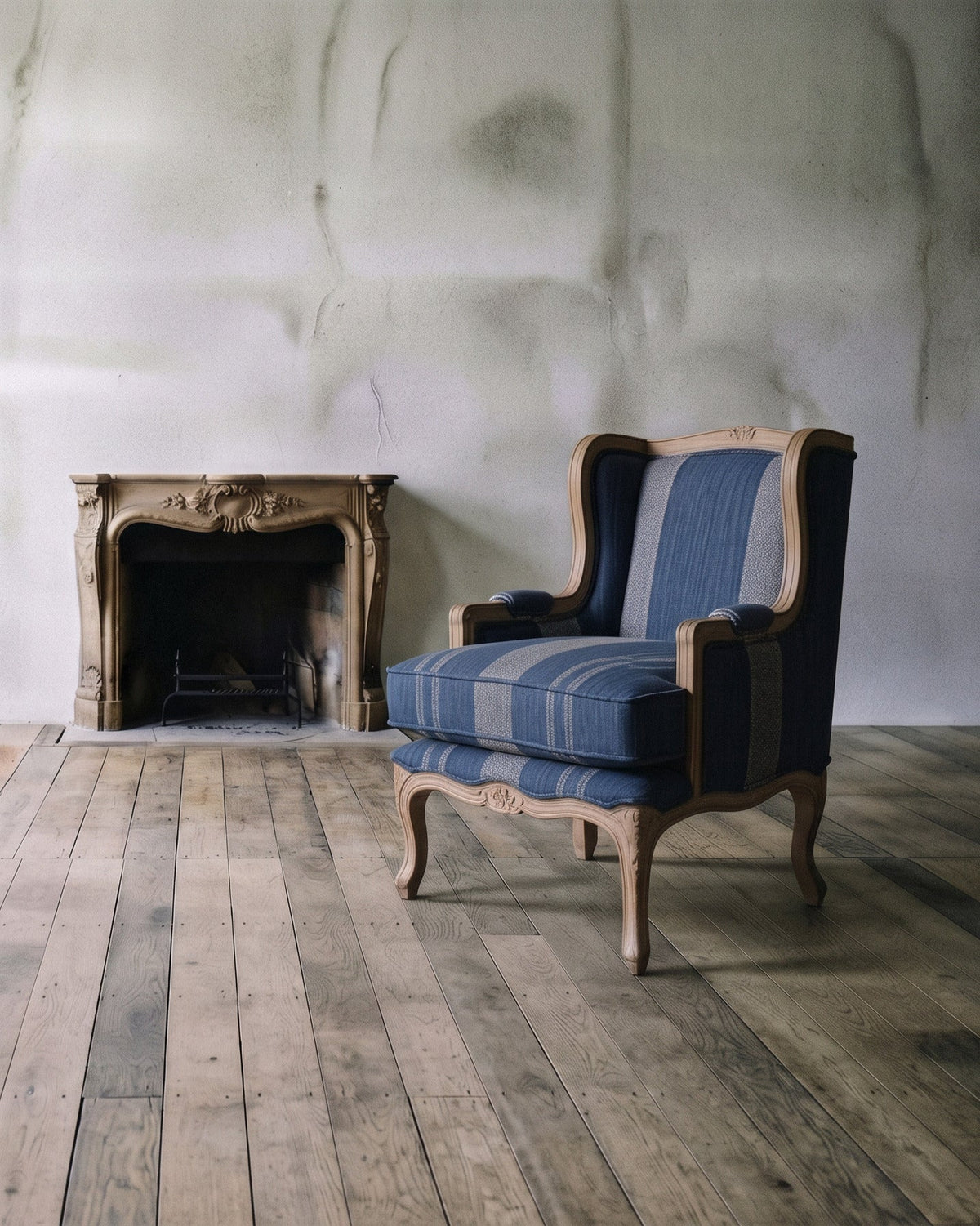 Bramley House accent chairs: a blue striped wingback armchair beside a carved stone fireplace on wide-plank wood floors.