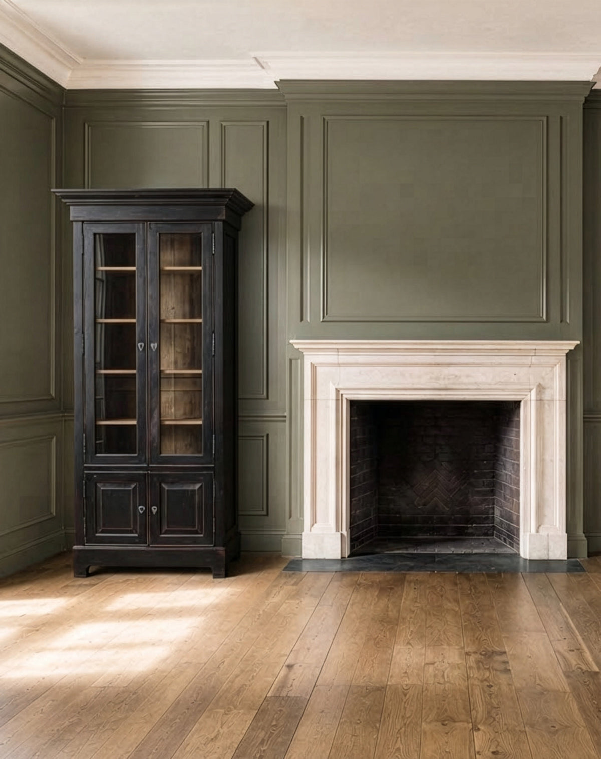 Bramley House bookcases and cabinets: a glazed two-door cabinet with open shelving beside a stone fireplace in a panelled room.