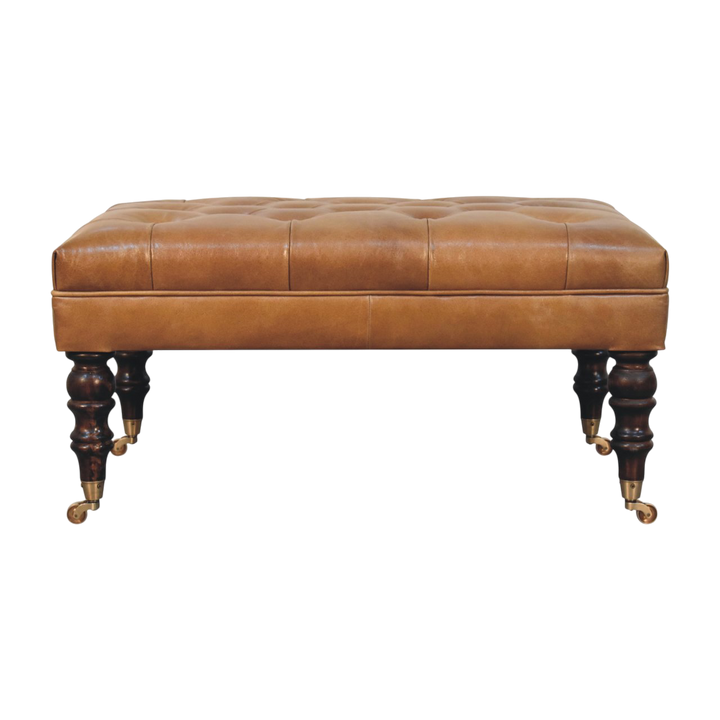 Sussex Leather Ottoman in Burnt Caramel, front view. Button-tufted caramel leather on turned chestnut legs with brass castors.